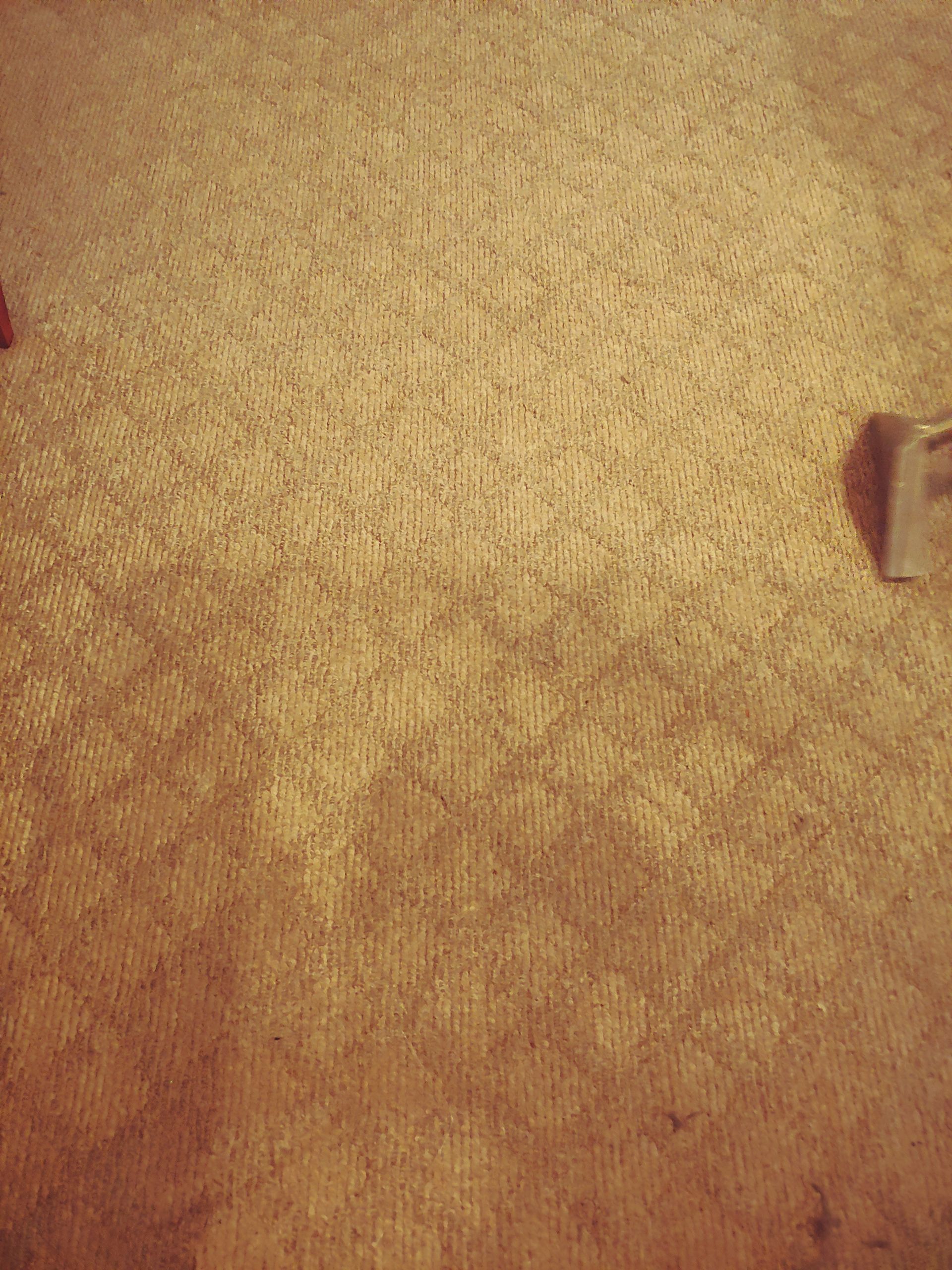Tan carpet with diamond-shaped pattern, possibly on a floor. Faded color.
