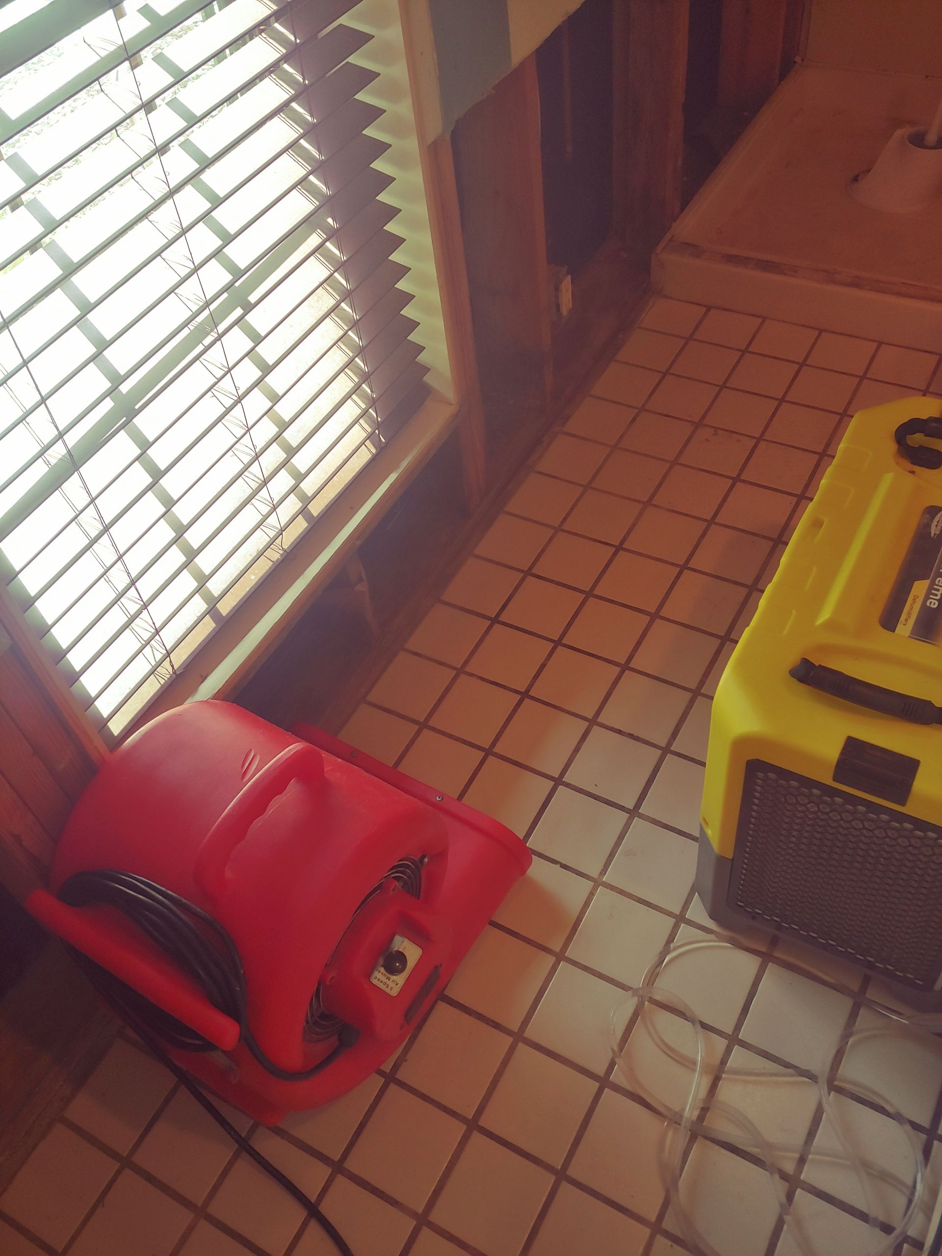 Red and yellow air movers on tiled floor near window with blinds, likely drying a flooded area.