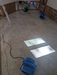 Interior room being dried, fans on the floor. Walls partially open, concrete floor, light shining through.