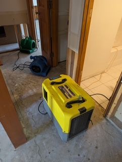 Three dehumidifiers inside a room with exposed wall studs; concrete floor, and doorway.