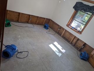 Room with exposed wall studs, concrete floor, drying fans, and a window.