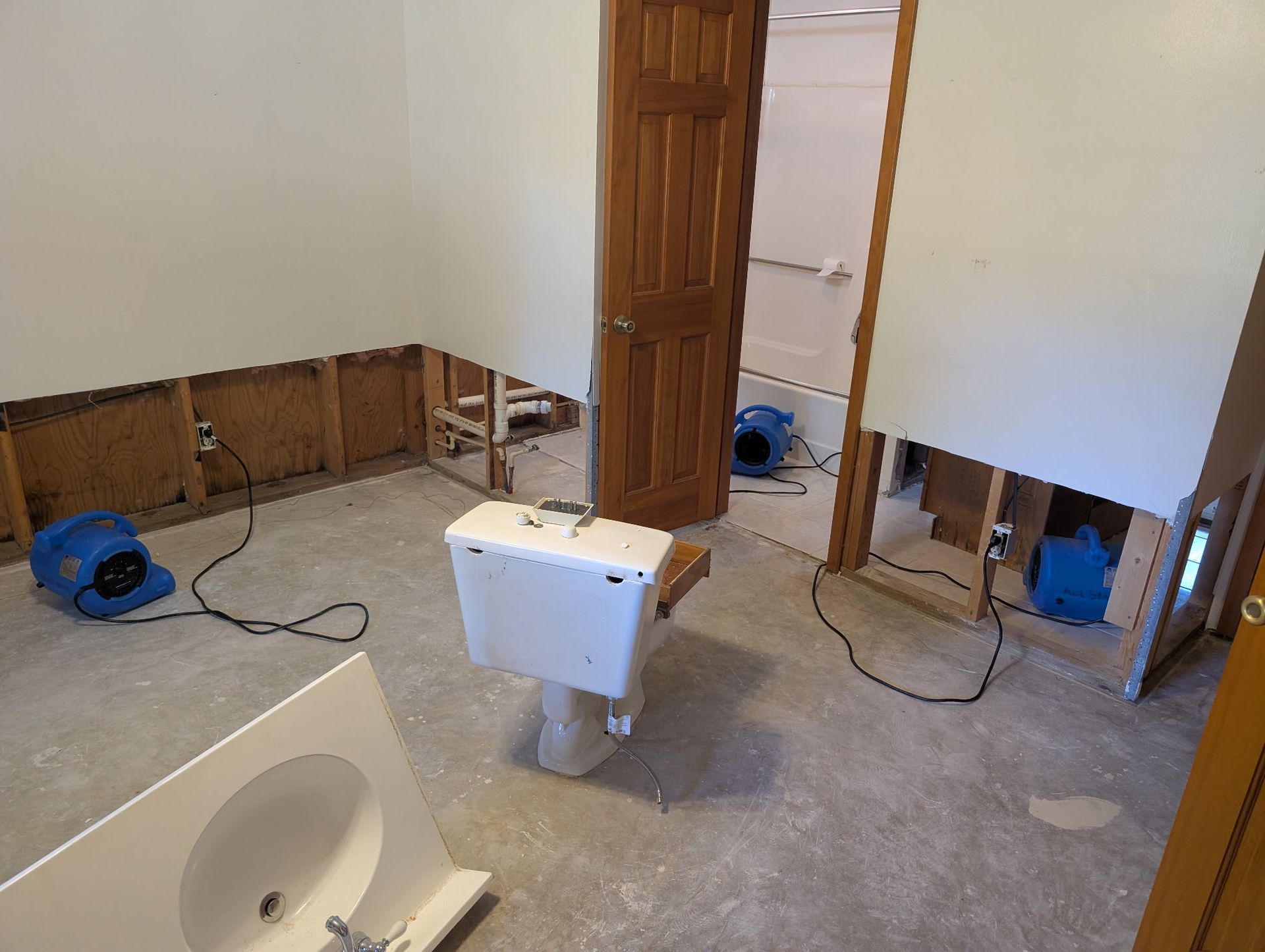 Bathroom renovation with exposed wall studs, toilet, sink, and air movers.