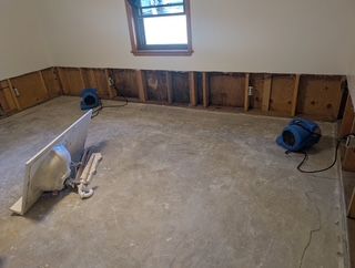 Room with exposed wall studs, concrete floor, drying fans.