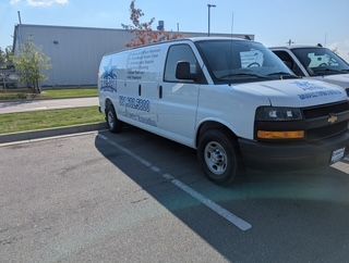 White van with company logo parked in a parking lot. Building and sunny sky in the background.
