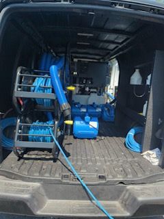 Inside a van, blue cleaning equipment: hoses, tanks, and a pump.