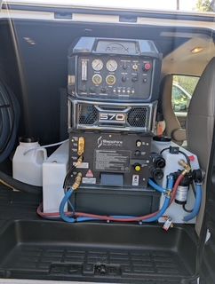Carpet cleaning equipment in a van: multiple stacked machines, hoses, and tanks.