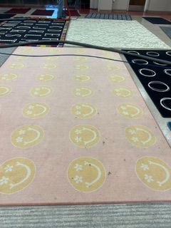 Variety of colorful rugs displayed on a floor, including a pink rug with repeating smiley face patterns.