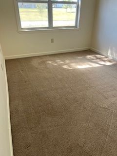 Empty room with tan carpet, window, and off-white walls.