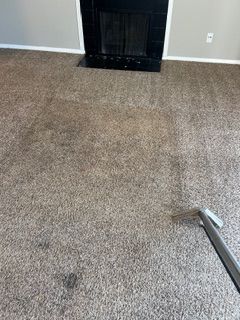 Carpet being cleaned with a cleaning tool, in front of a fireplace.