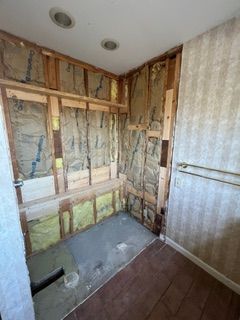 Bathroom undergoing renovation; exposed insulation, studs, and concrete floor; partially-removed walls.
