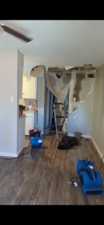 Room undergoing water damage restoration, fans drying floors, damaged ceiling.