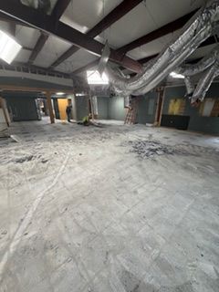Empty interior space during construction. Concrete floor, exposed beams, and a person in doorway.