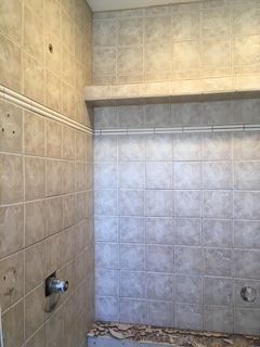 Tiled shower stall with beige square tiles and plumbing fixtures visible.