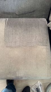Couch cushion cleaned on half. Light and dark gray sections show difference. A foot and a vacuum head are visible.