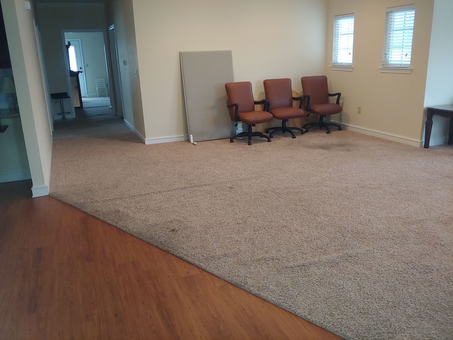 Room with hardwood floor and carpet. Three chairs face windows. Board leans against wall.