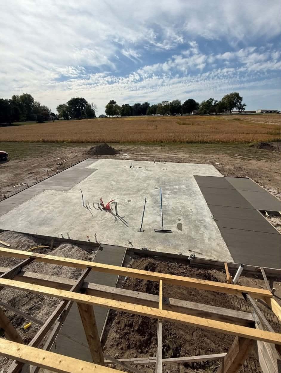 Concrete foundation slab at a construction site with open field and cloudy sky in the background