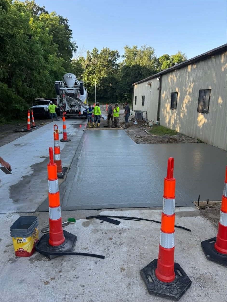 Fresh concrete driveway beside a building, with workers and orange traffic cones during roadwork.