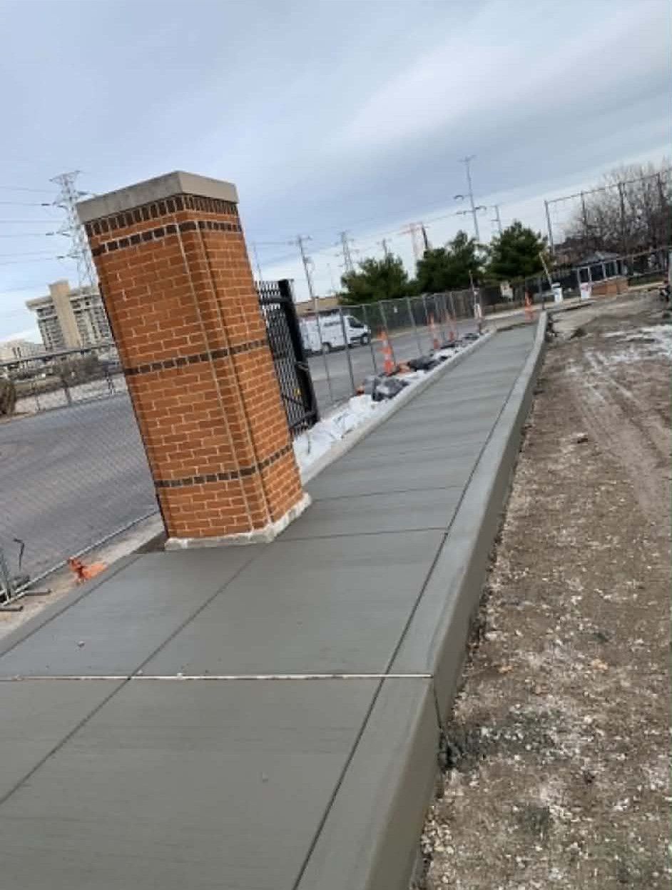 New concrete sidewalk beside a brick pillar along a roadside construction area