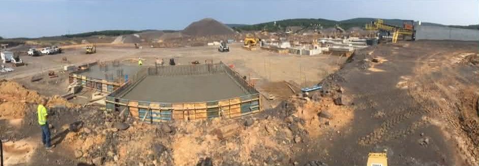Construction site with concrete foundation, workers, and excavators in a barren landscape