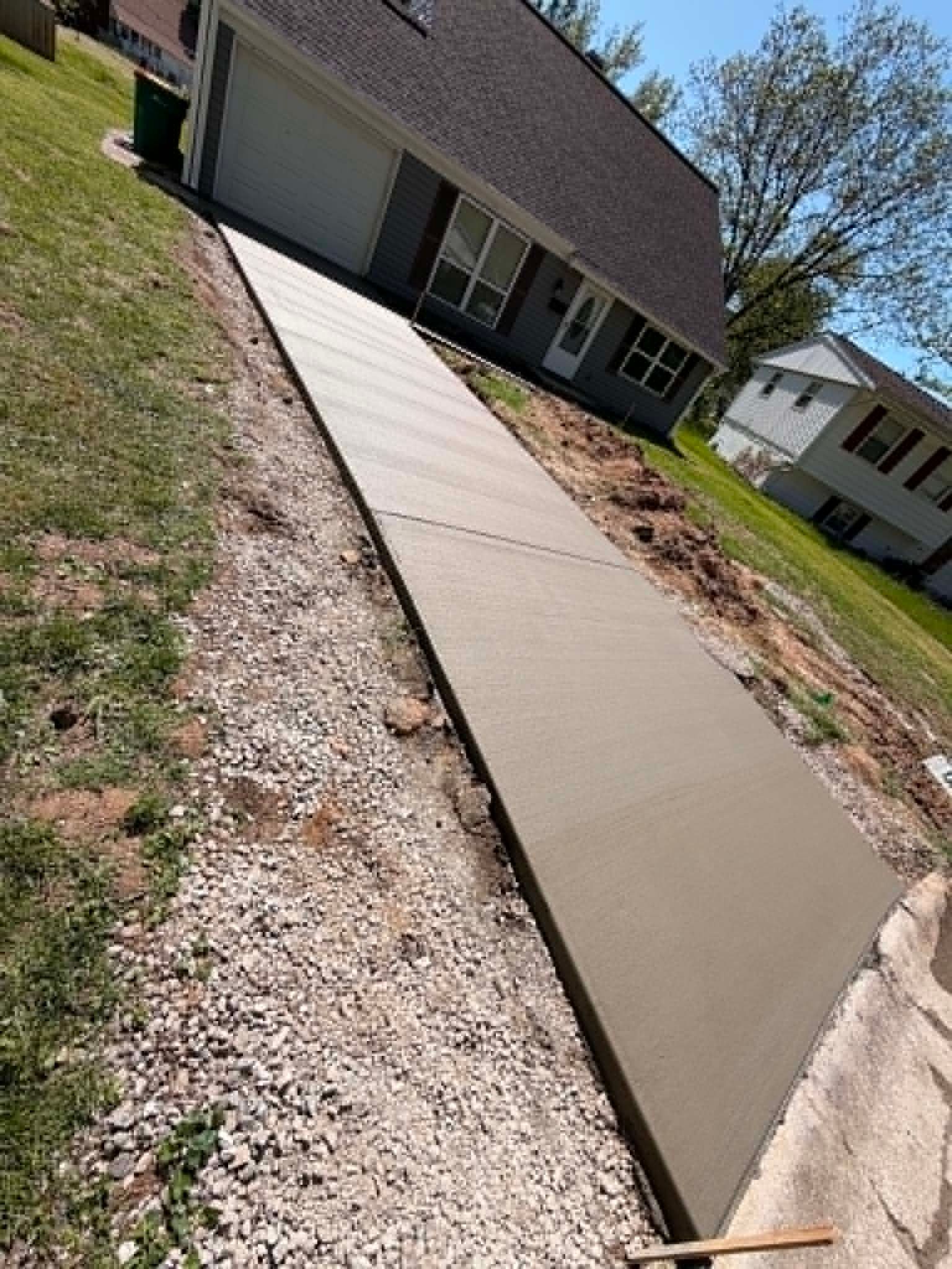 New concrete sidewalk ramp leading to a garage, with gravel edges beside a house