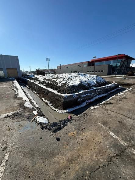 Snow-covered raised planter in an empty parking lot under a clear blue sky.