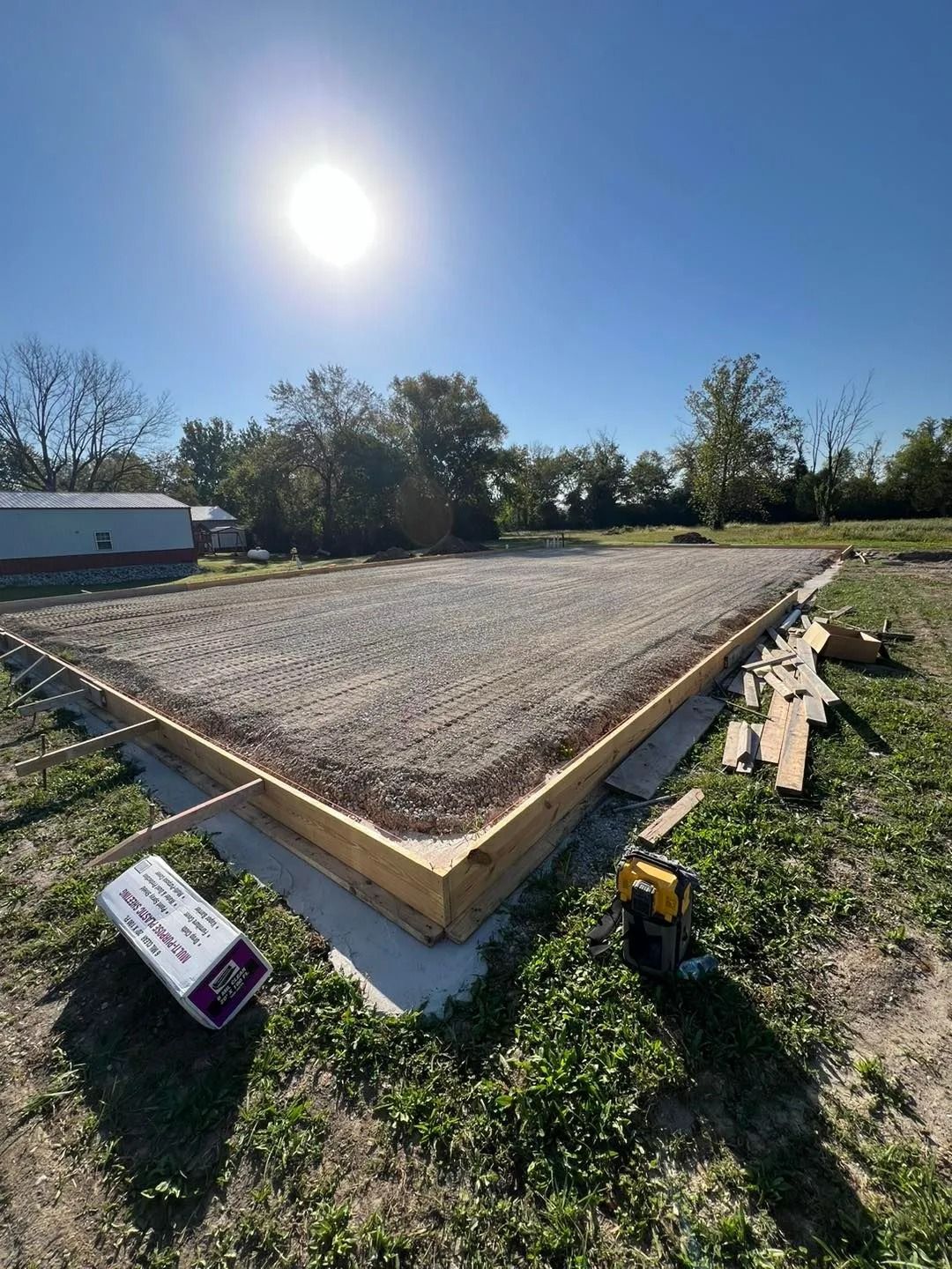Construction site: gravel-filled foundation with wooden formwork, clear sky, sunny day.