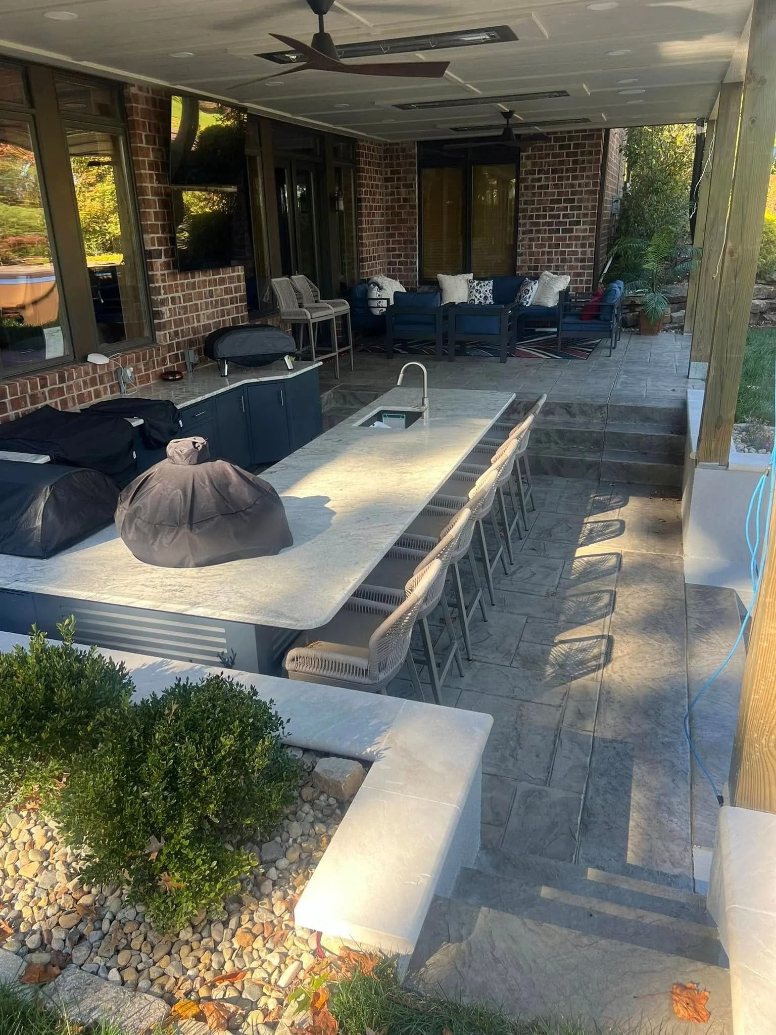 Outdoor patio with seating, fireplace, and overhead fan. Concrete and brick construction.