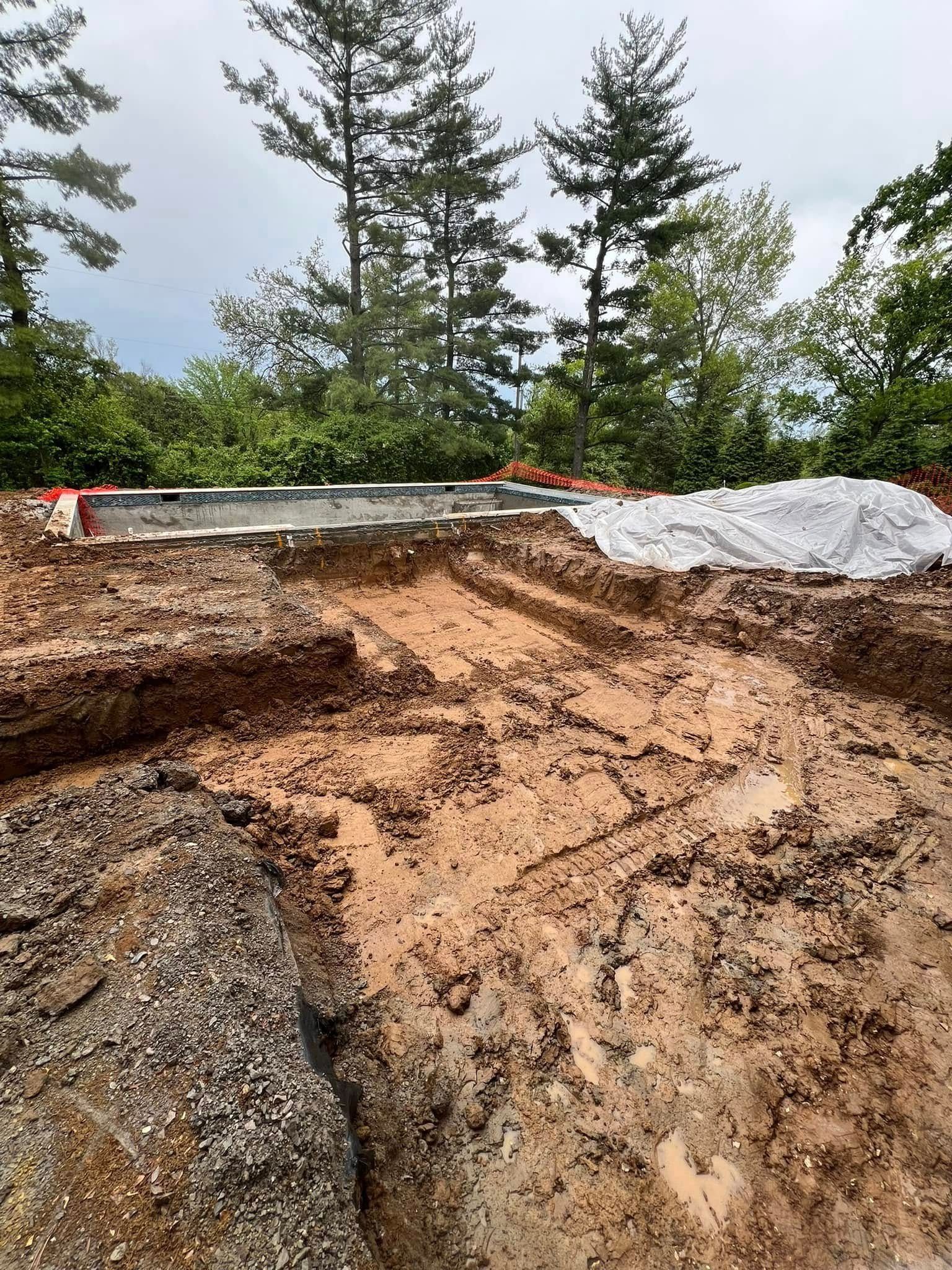 Construction site with a muddy, excavated area and a concrete foundation in a wooded environment.