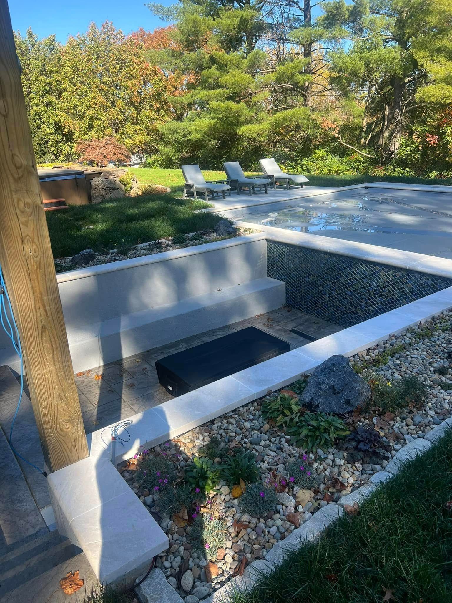 Backyard with pool, landscaping, and lounge chairs. Sunny day, green grass, and trees in the background.