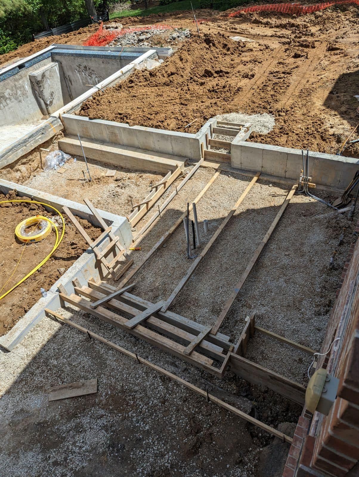 Construction site with concrete forms for steps and patio, surrounding a swimming pool. Brown dirt and gravel.