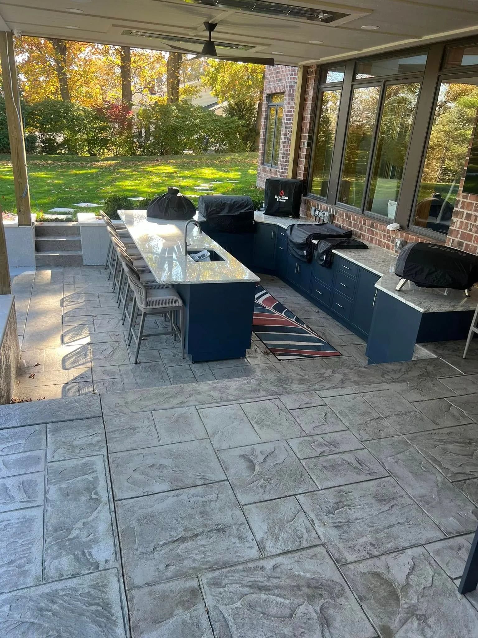 Outdoor kitchen with blue cabinets, gray countertops, and stamped concrete patio.