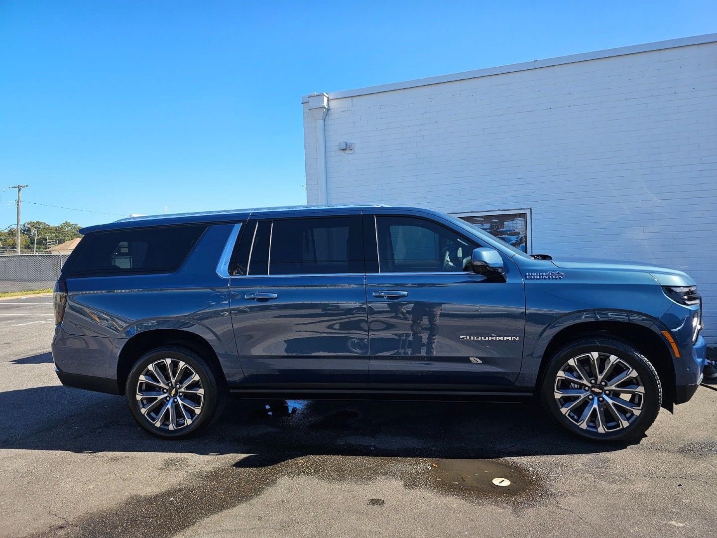 Blue Chevrolet Suburban parked in front of a white building on a sunny day.