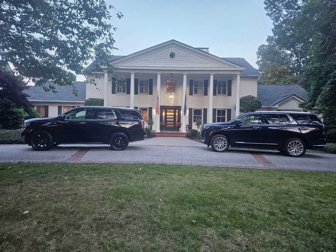 Two black SUVs parked in front of a white mansion with columns.