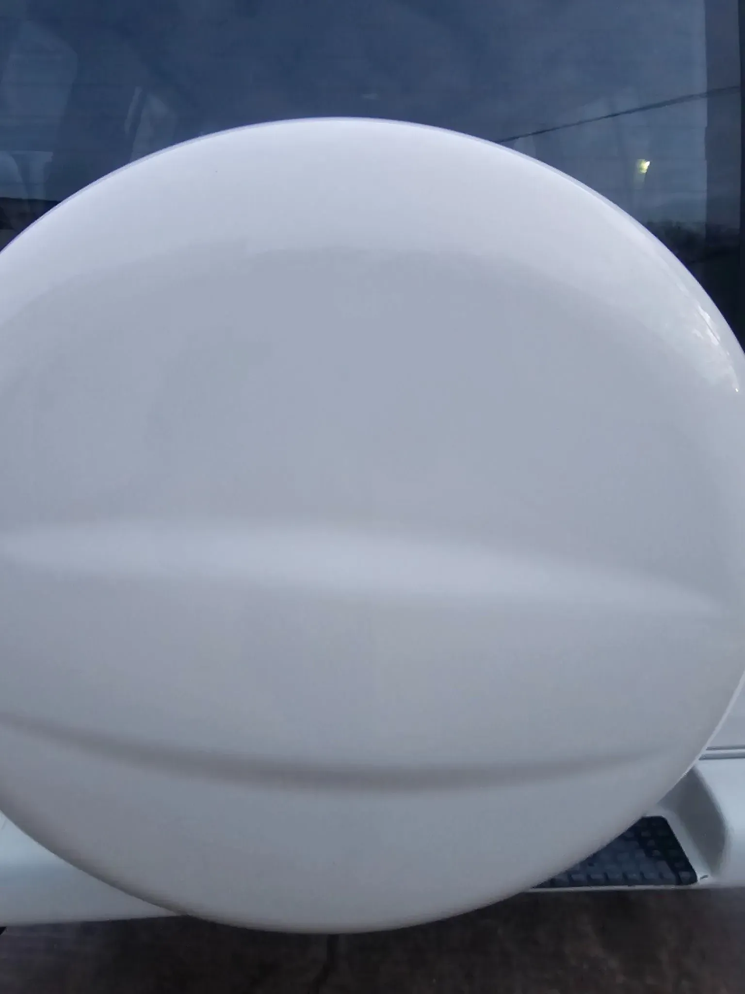 A smooth, white, circular spare tire cover mounted on the back of a vehicle.