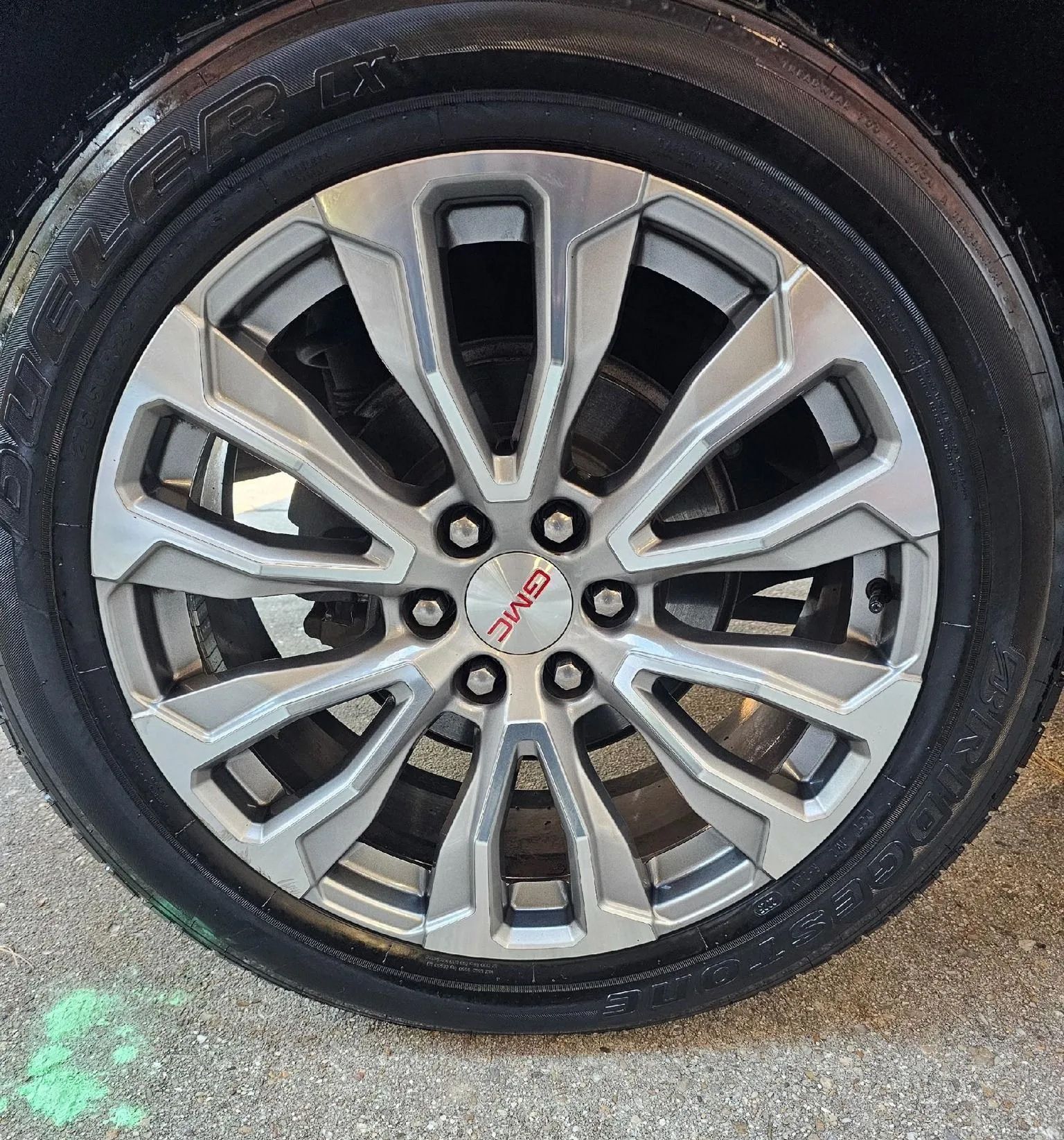 A close-up of a silver GMC multi-spoke alloy wheel with a black tire, viewed from the side.