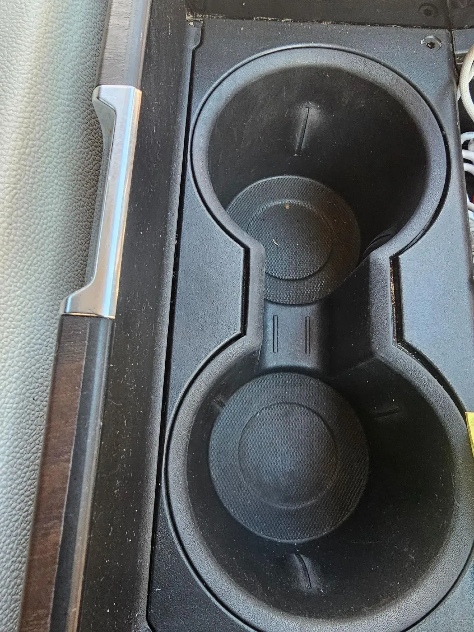 A close-up, top-down view of a dual-cup holder in a vehicle's center console with a black textured rubber lining.