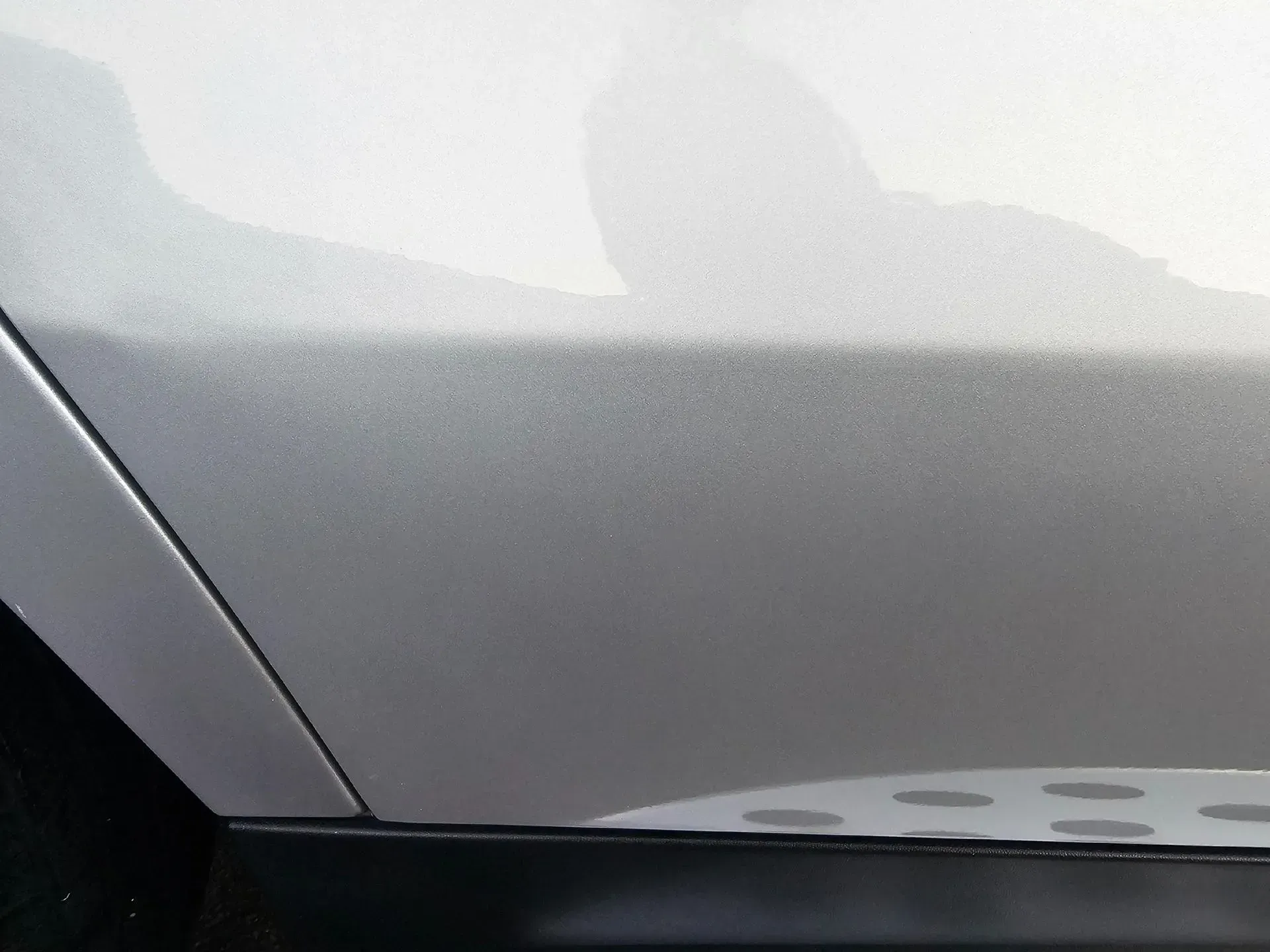 Close-up view of a metallic silver car door panel with a black trim piece along the bottom edge.