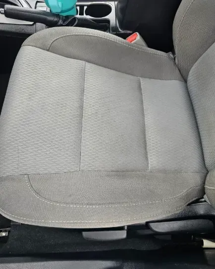 A grey fabric car seat viewed from above, with a cup holder and parking brake lever visible in the background.