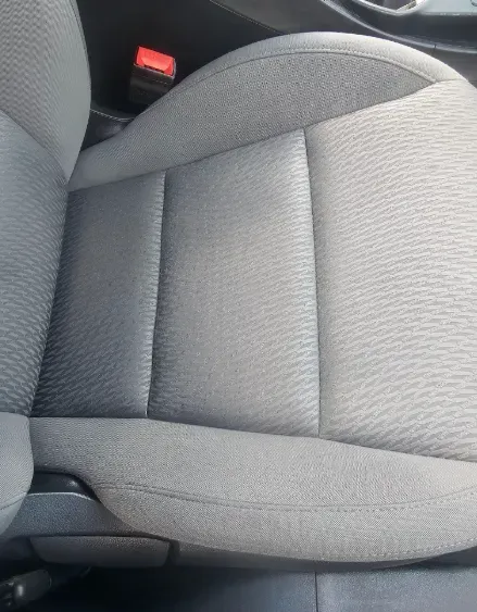 A close-up view of a car seat with grey fabric upholstery and a black leather-textured panel on the side.