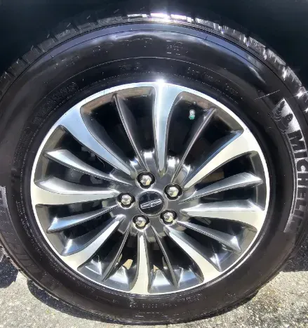 A close-up of a silver and gray multi-spoke alloy car wheel with a Michelin tire, viewed from the side.