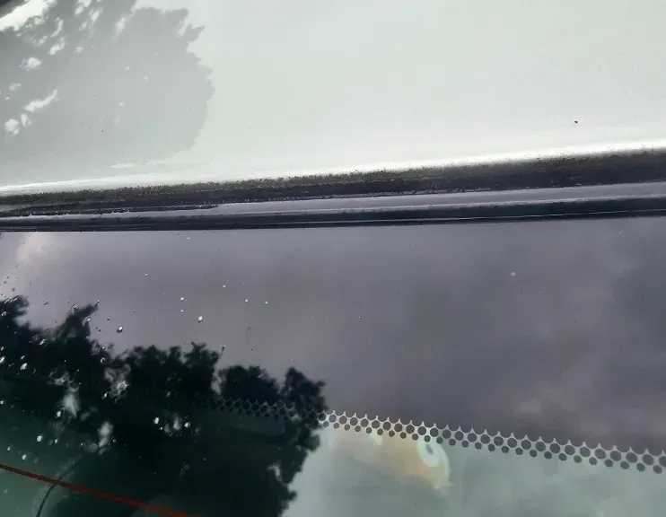 Close-up of a car window showing moisture beads and a black rubber seal against a white vehicle frame.