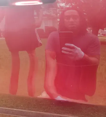 A person holding a phone for a reflection selfie in the red, glossy paint of a vehicle.