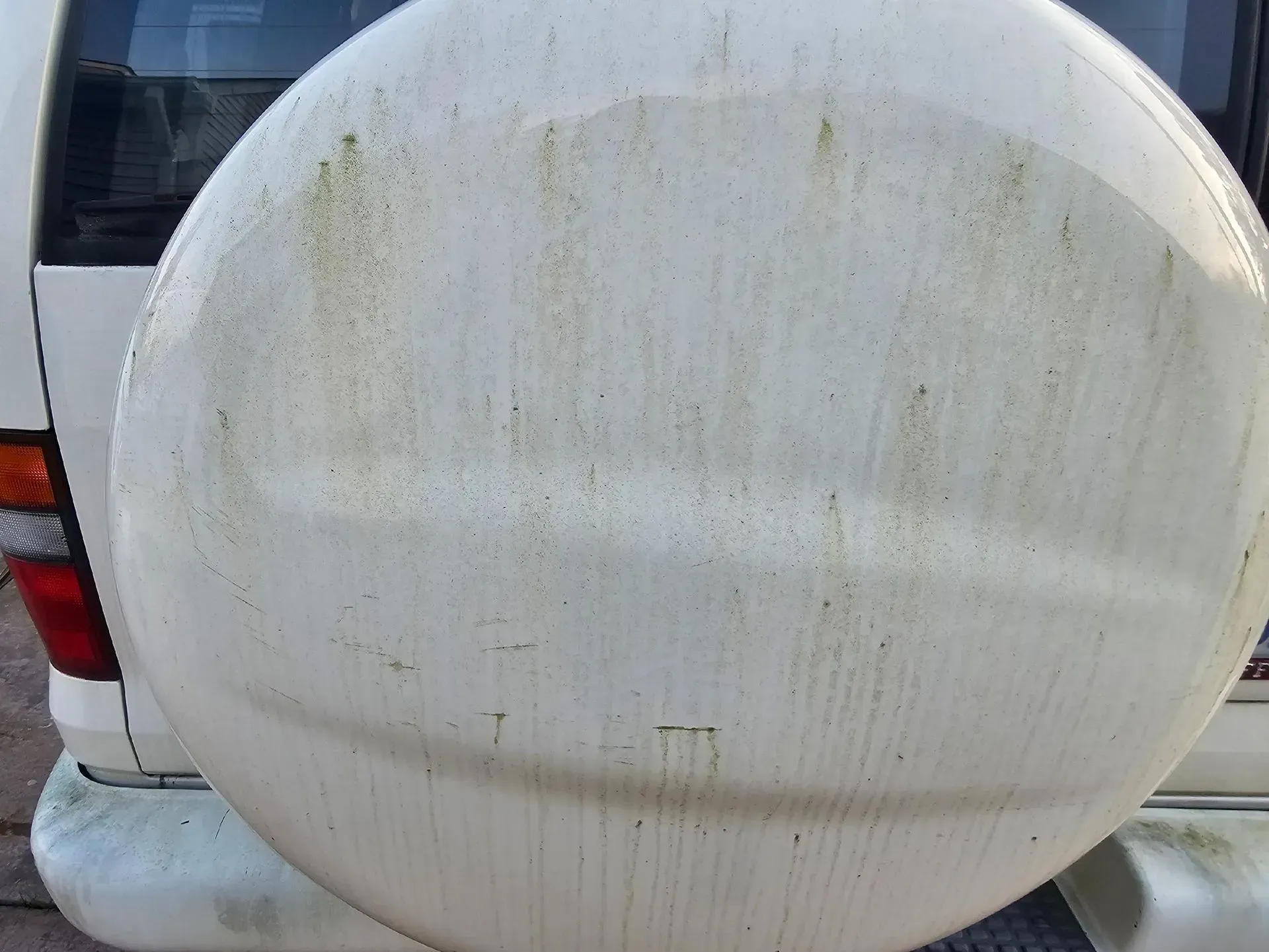 A dirty white spare tire cover mounted on the back of a white vehicle.