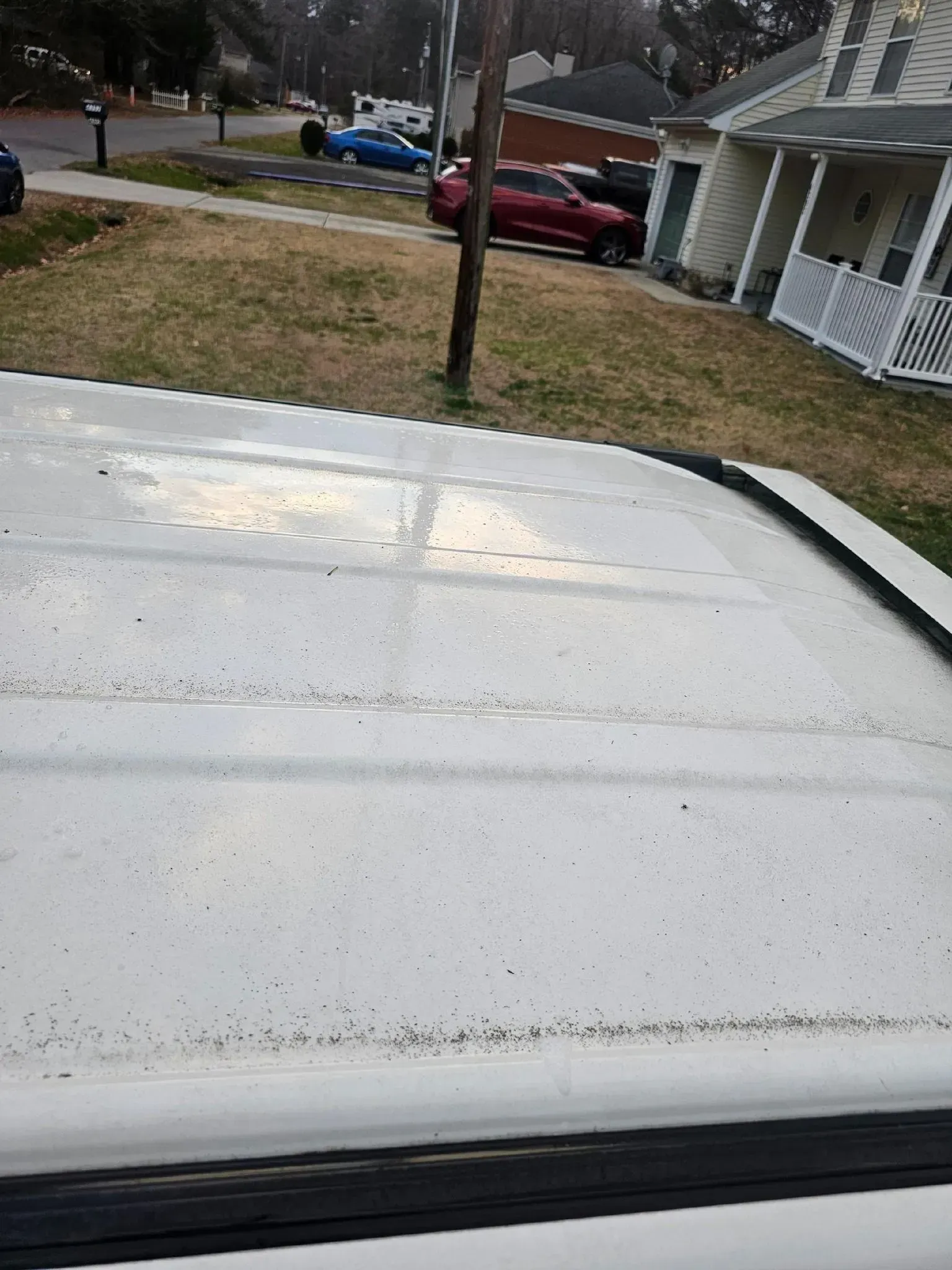 White vehicle roof covered in fine grit or dust, with a residential street and house visible in the background.