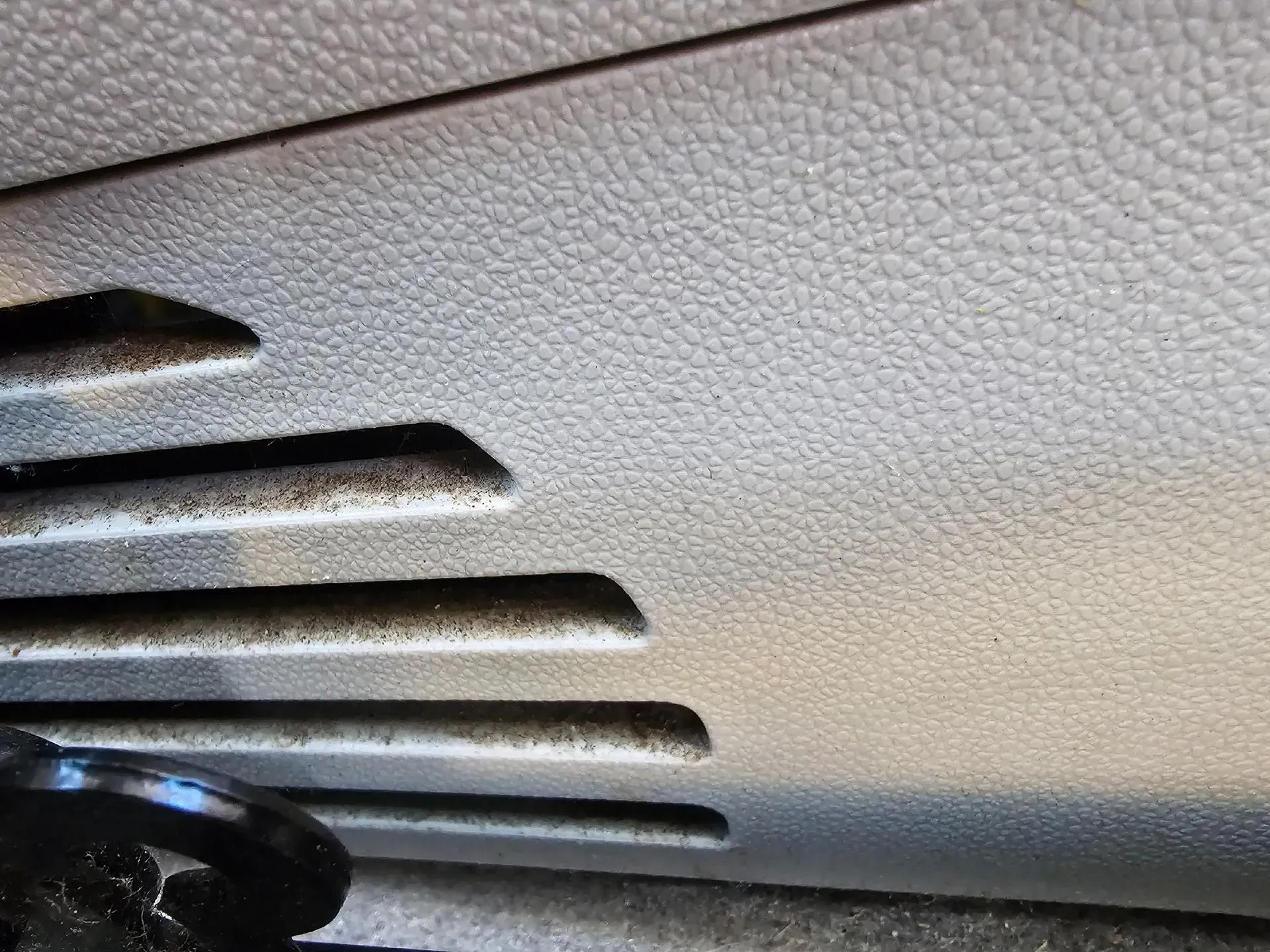 Close-up of a dusty, light gray plastic car interior panel featuring several horizontal ventilation slats.