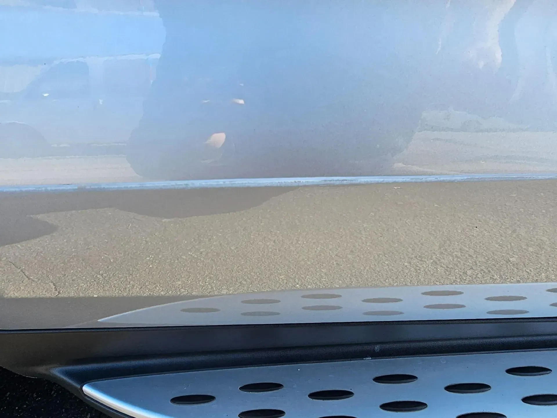 Close-up of a vehicle's side step and reflective lower body panel showing a distorted reflection of a nearby car.