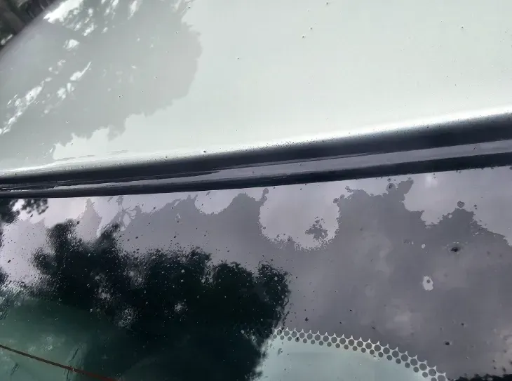 A close-up view of a car window showing streaks, water spots, and moisture residue on the glass surface.