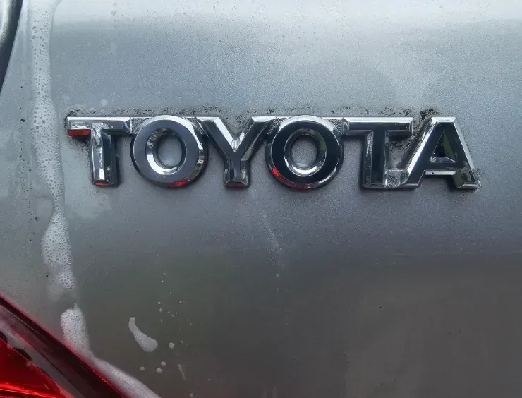 Chrome Toyota emblem on a silver car surface, with soapy water streaks running down the panel.