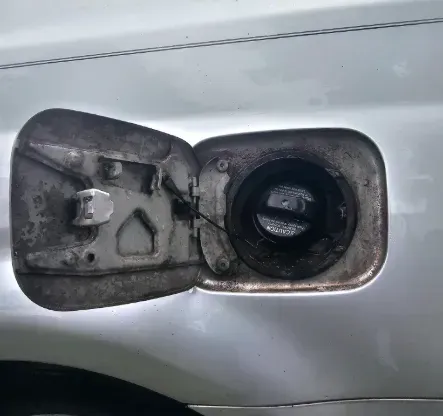 Open silver car fuel door with a black fuel cap visible inside the filler neck.