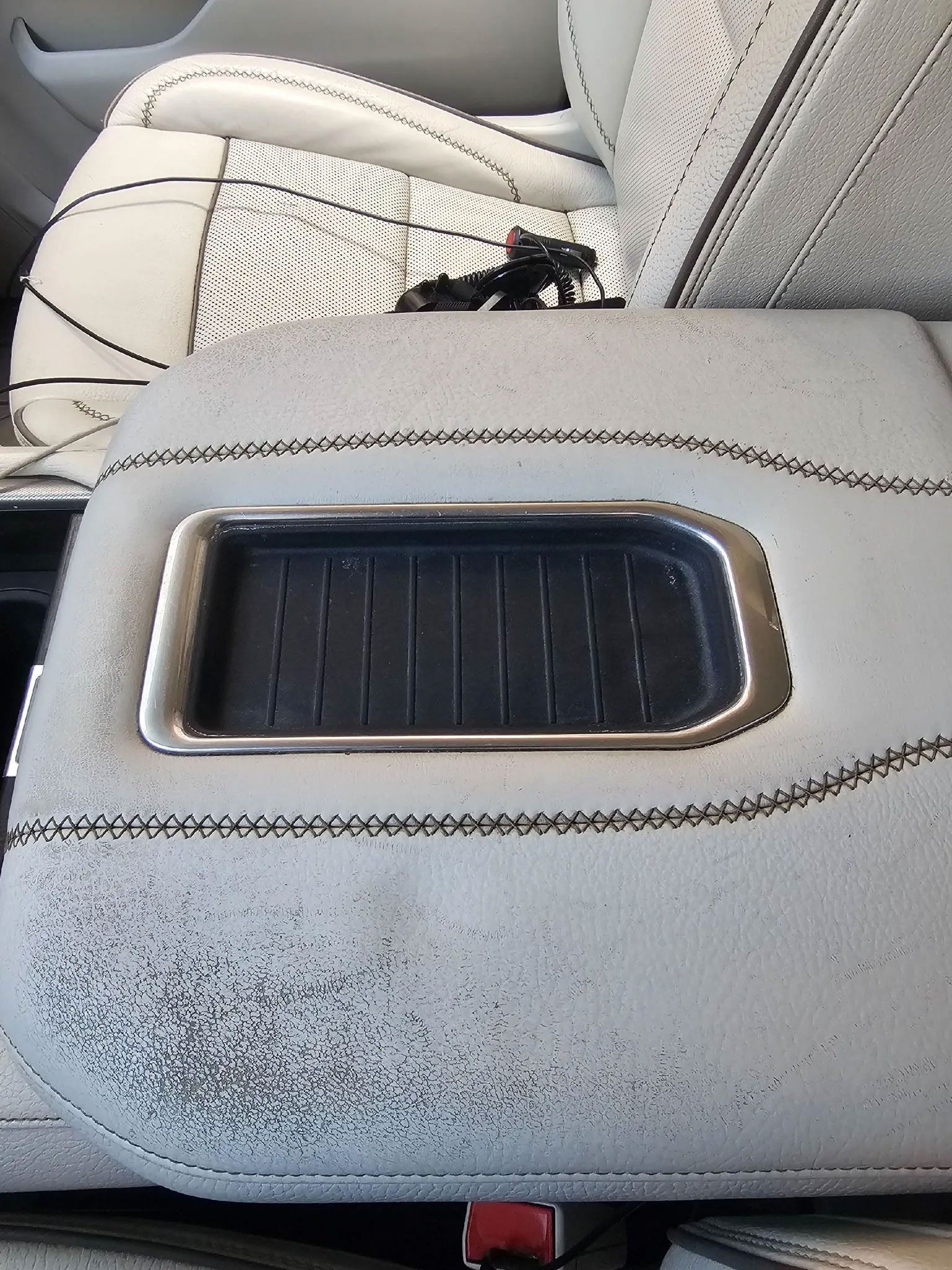 Gray car console with a silver-rimmed storage compartment and detailed stitching.